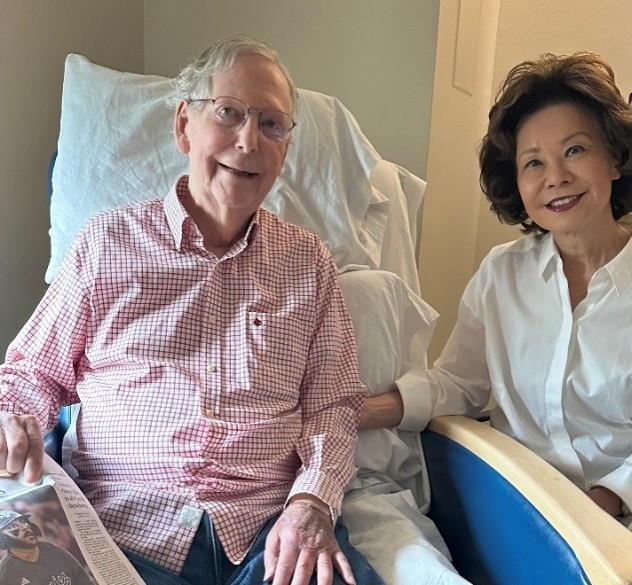 Mitch McConnell seated in a rehabilitation facility beside Elaine Chao and holding a newspaper in a photograph released by his office on July 12, 2026.